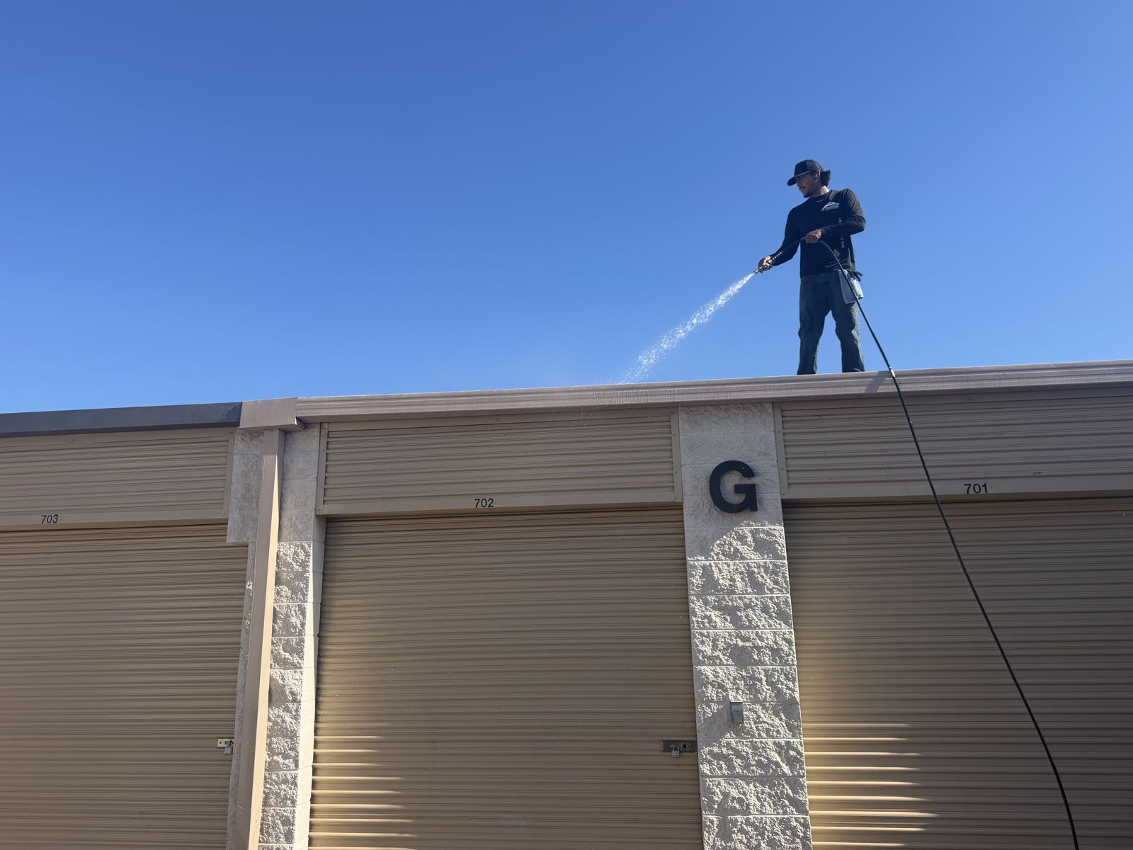 Technician pressure washing an industrial building roofline